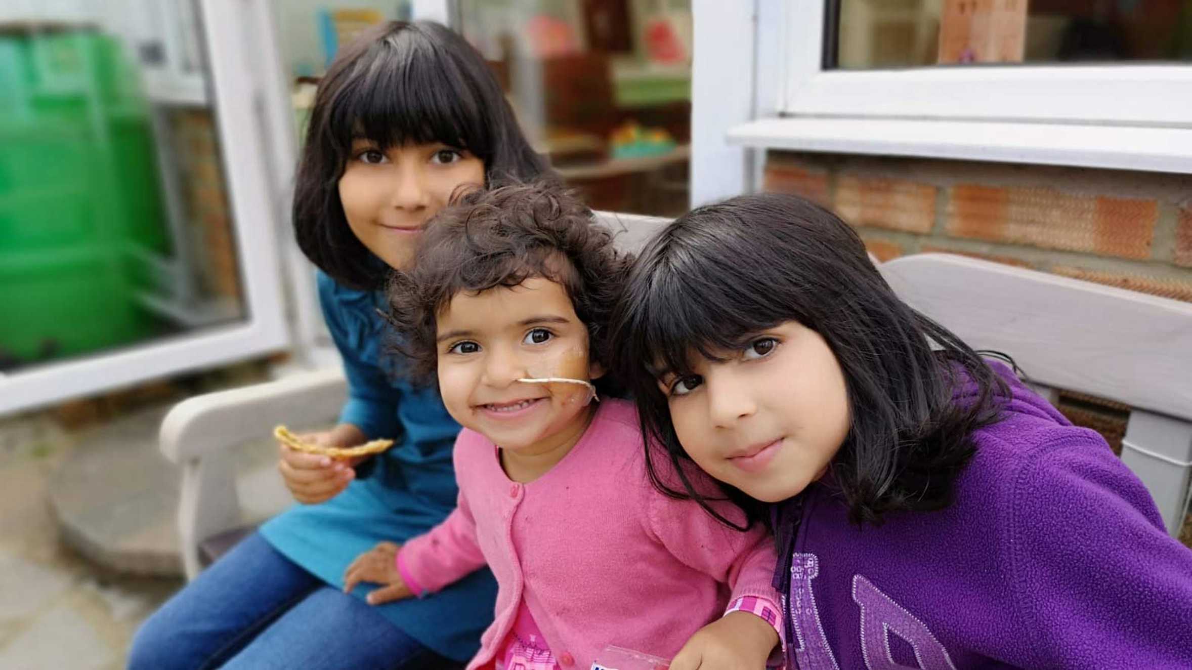 Sophia and her sisters sitting together on a garden bench.