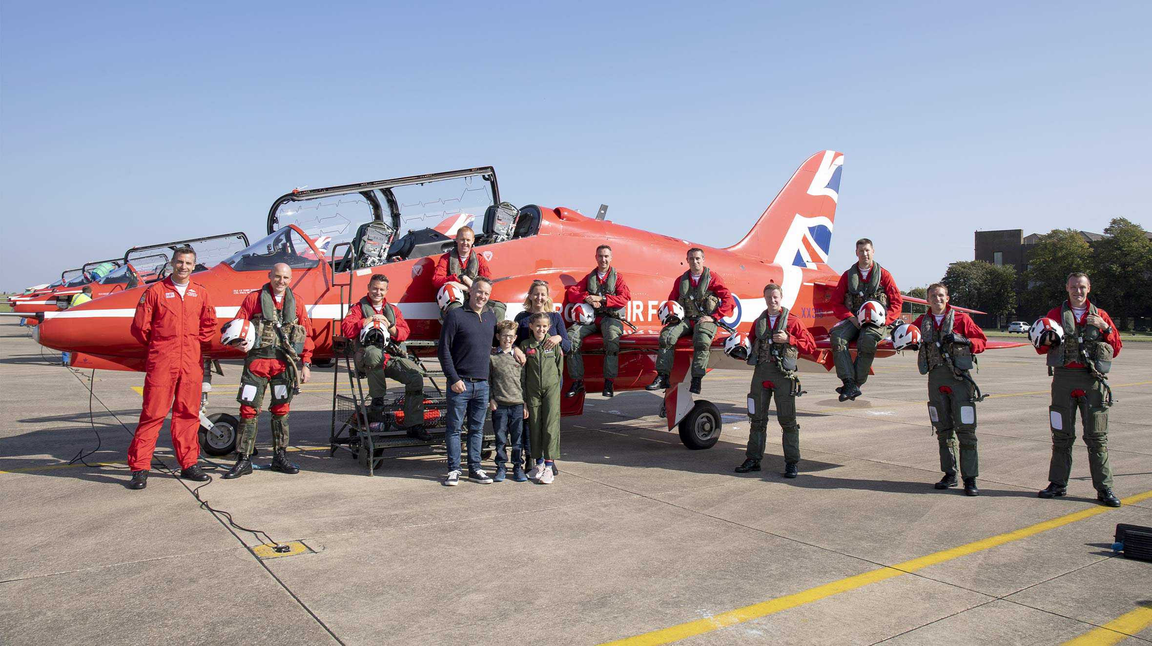 John and his family posing in front of a Red Arrows jet with the pilots and ground crew.