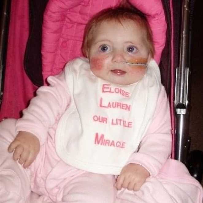 A young Eloise in pink pyjamas with a bid embroidered with the words ' Eloise Lauren our little miracle'.