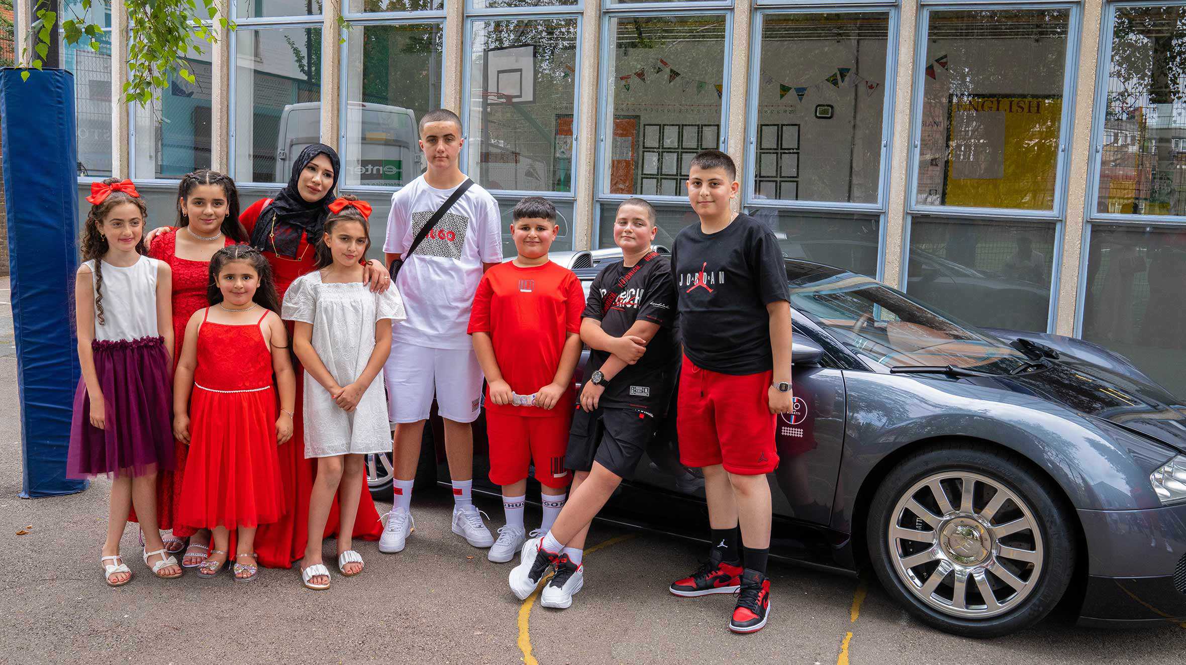 Adil, standing with his family and friends in front of a Bugatti Veyron supercar.