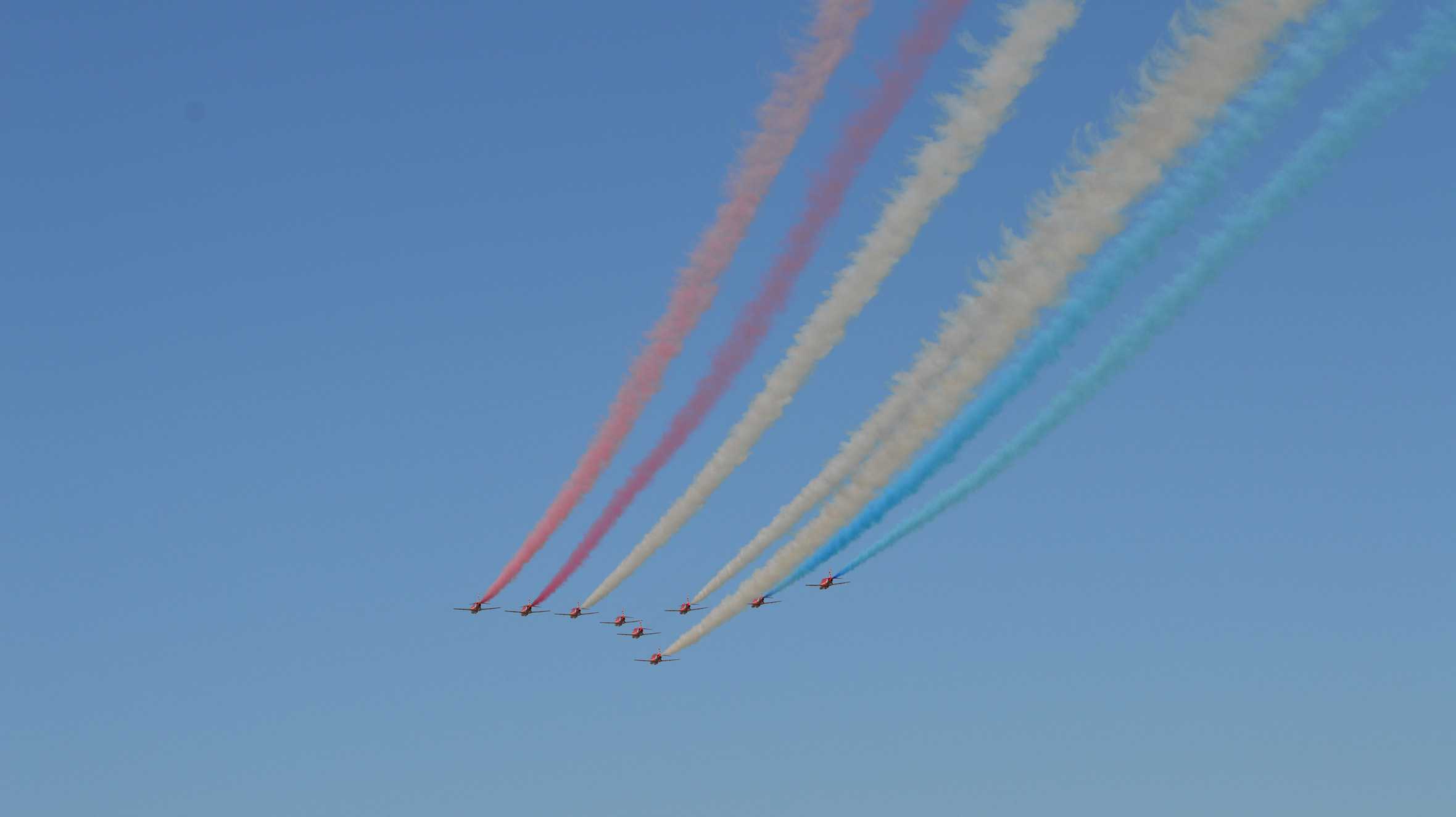 A formation of Red Arrows jets leaving a red, white and blue smoke trail across the sky.